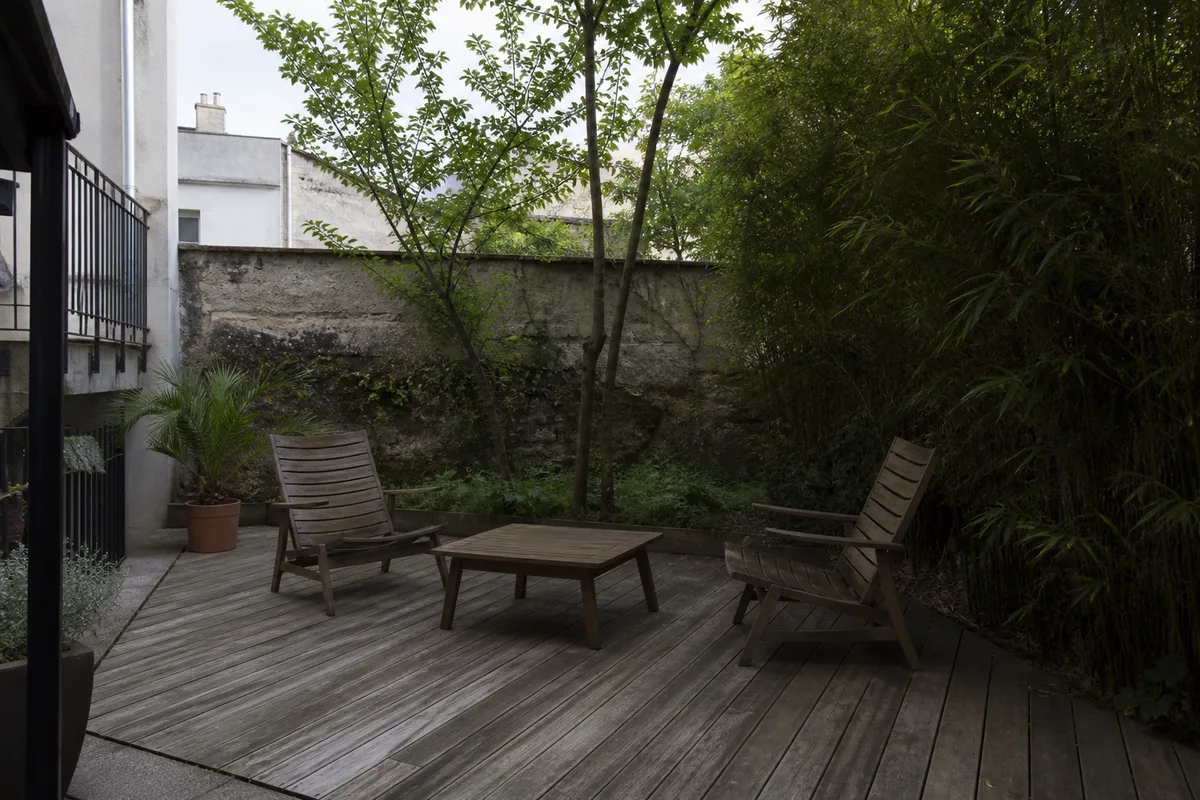 Terrasse en lames de bois clair dans un petit jardin de ville nantais, mobilier simple, lumière d&rsquo;après-midi